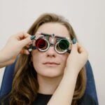 Unrecognizable female doctor correcting ophthalmic glasses selecting lenses on eyes of female patient during appointment in clinic against white wall